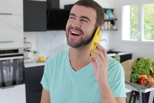 portrait of handsome young man talking by phone at kitchen at home - Photo, image