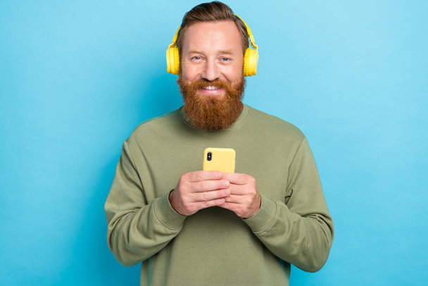 Photo of good mood satisfied guy with ginger hairstyle dressed khaki long sleeve hold smartphone isolated on teal color background. - Фото, изображение