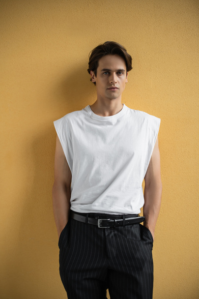 stylish man in white t-shirt and striped trousers standing near yellow wall  - 写真・画像