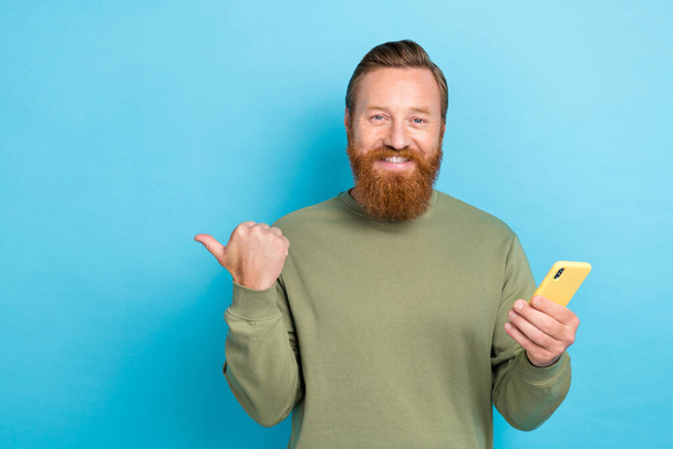 Portrait of handsome positive guy with ginger hairdo wear khaki pullover directing empty space isolated on turquoise color background. - Foto, Imagem