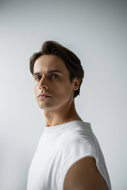 portrait of brunette man with blue eyes looking at camera while posing isolated on grey  - Photo, Image