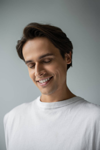 portrait of happy man in white t-shirt smiling isolated on grey  - Foto, Bild