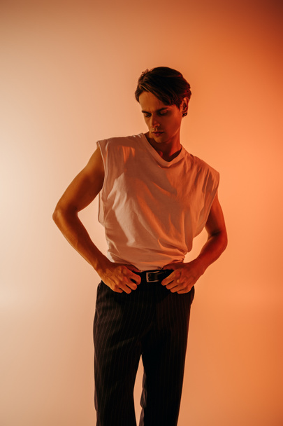 stylish man in white t-shirt and black pants posing on orange with gradient  - Fotografie, Obrázek