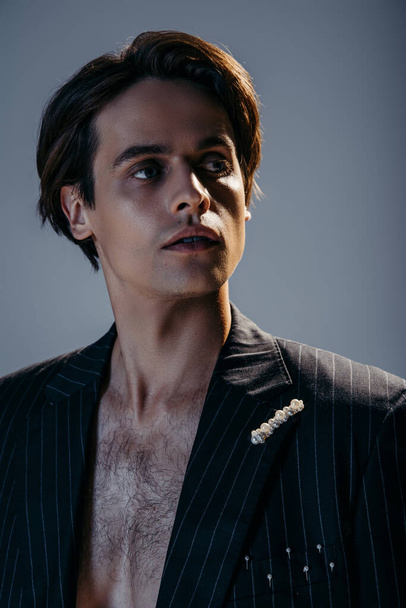 portrait of brunette man with hairy chest and stylish blazer on dark grey - 写真・画像