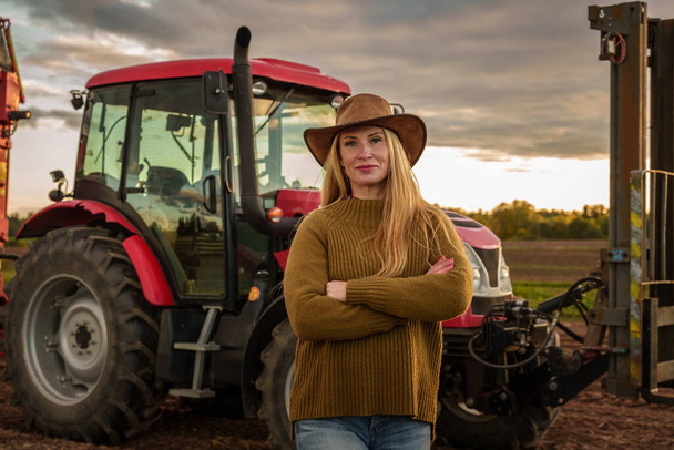 Portrait of confident farmer woman and modern combine on cultivated field. - Photo, Image