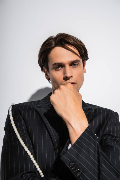 brunette man in trendy blazer with pearls posing while looking at camera on grey - Foto, immagini