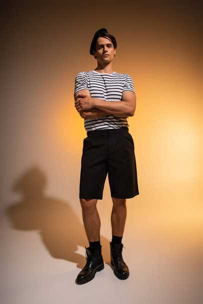 full length of man in beret and striped t-shirt standing with crossed arms on orange  - Foto, immagini