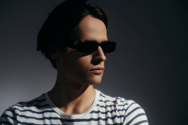 Portrait of stylish man in sunglasses posing isolated on grey with lighting  - Foto, Imagem