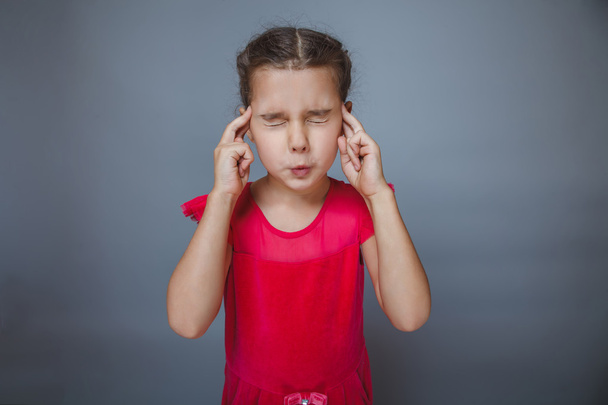 Girl covering her ears and eyes in a red dress on gray backgro - 写真・画像