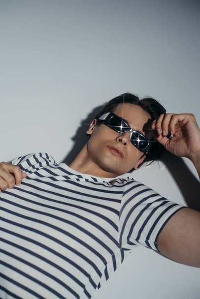 Wysoki kąt widzenia modny model w okularach przeciwsłonecznych i t-shirt leżący na szarym tle z oświetleniem  - Zdjęcie, obraz