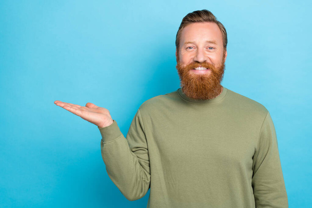 Photo of positive cheerful guy with red hairstyle dressed khaki long sleeve demonstrating empty space isolated on teal color background. - Foto, imagen