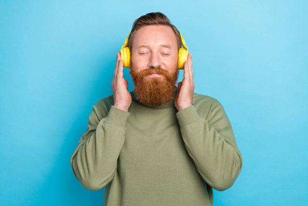 Photo of positive relaxed guy with ginger hairstyle dressed khaki long sleeve arms touch headphones isolated on teal color background. - Valokuva, kuva