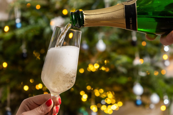 Verter champán en la copa, contra el árbol de Navidad, de cerca. Feliz año nuevo fiesta.  - Foto, imagen