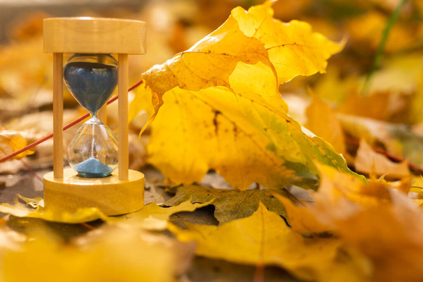 Őszi időtéma, Homokóra a lehullott leveleken különböző színekben másolási hellyel. - Fotó, kép