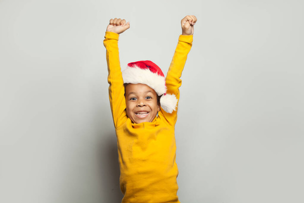 ¡Un niño negro gana-gana! Niño en sombrero de Santa Divirtiéndose sobre fondo blanco - Foto, imagen