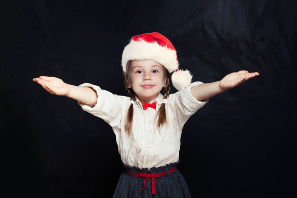 Little girl in Santa hat having fun on empty blackboard background with copy space - Photo, image