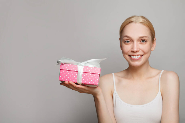 Χαμογελώντας όμορφη γυναίκα κρατώντας ροζ κουτί δώρου παρόν σε λευκό φόντο - Φωτογραφία, εικόνα