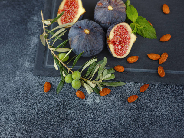 fresh ripe figs fruit almond nuts and olive branch on dark table. mediterranean food concept - Foto, Imagen
