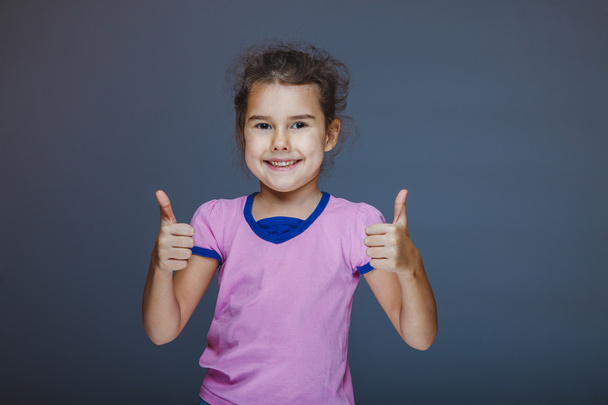 Girl showing thumbs up sign yes on a gray background - Foto, imagen