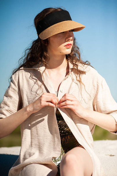 hermosa mujer joven en un sombrero y gafas de sol sentado en la playa - Foto, Imagen