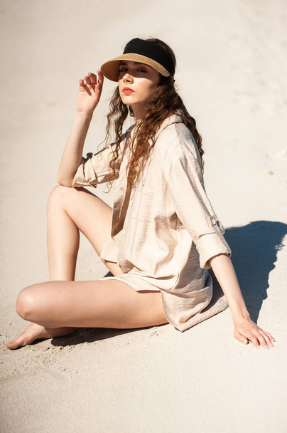 beautiful girl in a black dress and hat posing on the beach - Φωτογραφία, εικόνα