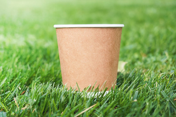 A paper cup on a background of grass. Brown cup for drinks. - Фото, изображение