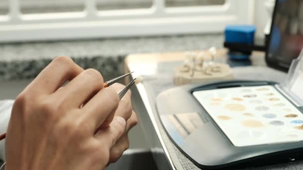 Zahntechniker färben Zahnersatz im Labor mit einem Pinsel ein. Ästhetische Färbung der Zähne. Konzept der Implantatproduktion. - Filmmaterial, Video