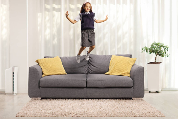 Girl in a school uniform jumping on sofa at home  - Φωτογραφία, εικόνα
