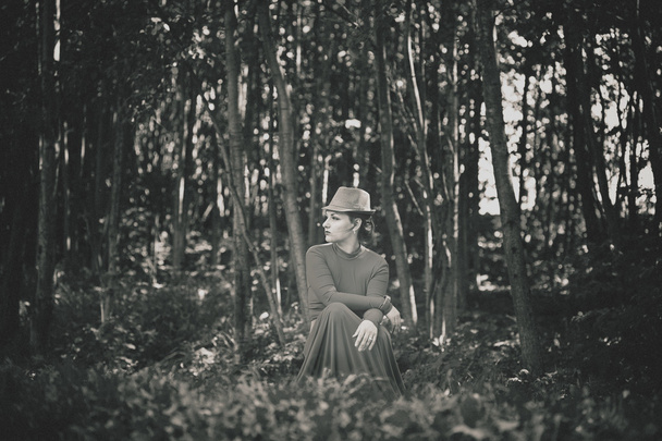Tyttö mekossa ja hattu päässä istuu hänen kummituksia metsässä. Kuva retrotyyliin
 - Valokuva, kuva