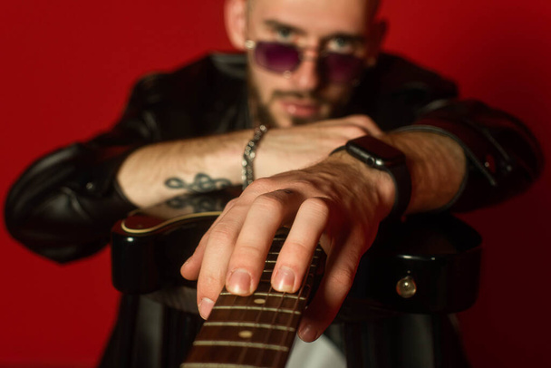 Tattooed rocker strums a guitar in the foreground. Red background. - Photo, Image
