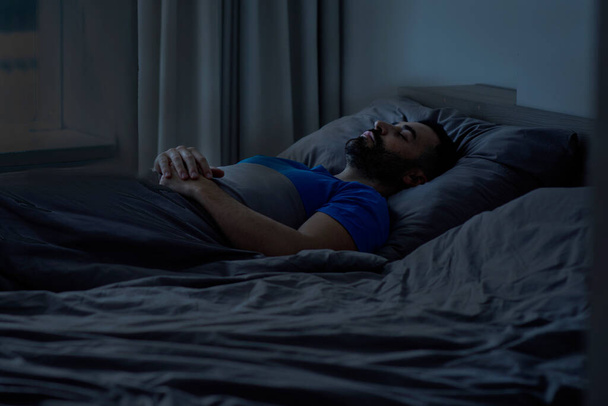Zijaanzicht van een jonge Europese man die goed slaapt en 's nachts in bed ligt. Hoge kwaliteit foto - Foto, afbeelding