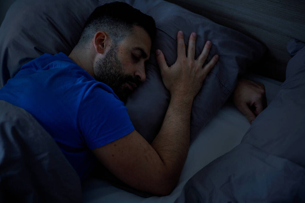 Een Italiaanse man in blauwe pyjama ontspant zich in een moderne slaapkamer, genietend van een gezonde nachtrust. zicht van bovenaf. Hoge kwaliteit foto - Foto, afbeelding