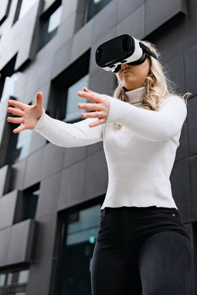 Blonďatá žena v technologii virtuální reality proti moderní futuristické budově. Nakupování v metaverzním obchodě. - Fotografie, Obrázek