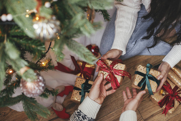 Καλά Χριστούγεννα και καλές γιορτές! Οικογενειακή ανταλλαγή χριστουγεννιάτικων δώρων κάτω από το χριστουγεννιάτικο δέντρο σε εορταστική διακοσμημένο δωμάτιο κοντά. Ζευγάρι χέρια ανταλλαγή με τυλιγμένα δώρα κορυφαία προβολή - Φωτογραφία, εικόνα