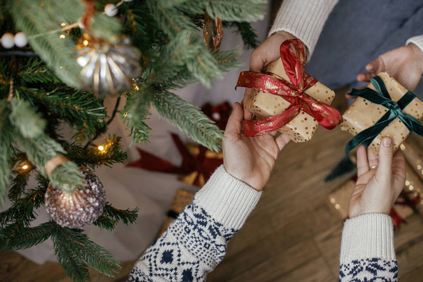 Merry Christmas and Happy Holidays! Family exchanging christmas gifts under christmas tree in festive decorated room close up. Couple hands exchanging with wrapped presents top view - Foto, Imagen