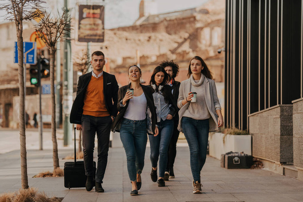 A group of diverse young businessmen on a break from work walk around the city, use smartphones, listen to music, and have fun.  - Foto, imagen