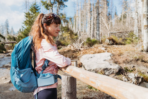 Ein junges Mädchen mit einem Wanderrucksack auf dem Rücken lehnt am Geländer und ruht sich aus. Wandern im Wald, Wandern und ein sportlicher Lebensstil. - Foto, Bild