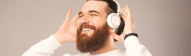 Close up panorama shot of a bearded man enjoying music through headphones. Studio photo. - Zdjęcie, obraz