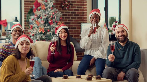 Portrait of diverse colleagues making toast with wine glasses, saying cheers to celebrate christmas eve in office. Drinking alcohol and feeling festive during xmas holiday season. - Photo, Image