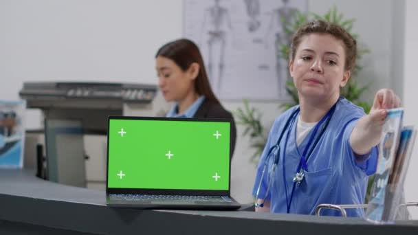 Enfermera y recepcionista trabajando con pantalla verde en el portátil en el mostrador de recepción de la instalación. Usando croma en blanco plantilla de la clave wth pantalla de fondo mockup aislado y copyspace en la pantalla de la PC. - Imágenes, Vídeo