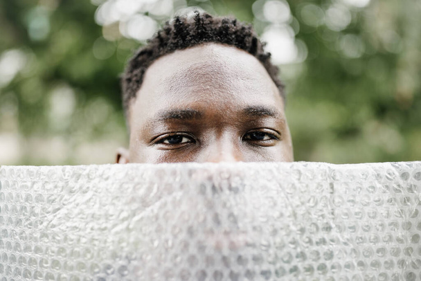 Nuori afroamerikkalainen mies ulkona, lähikuva katumuotokuva muovisella kuplamuovilla. Ekologia, ympäristökeskustelu, mielenterveyden käsite. Syksy tai kevät - Valokuva, kuva