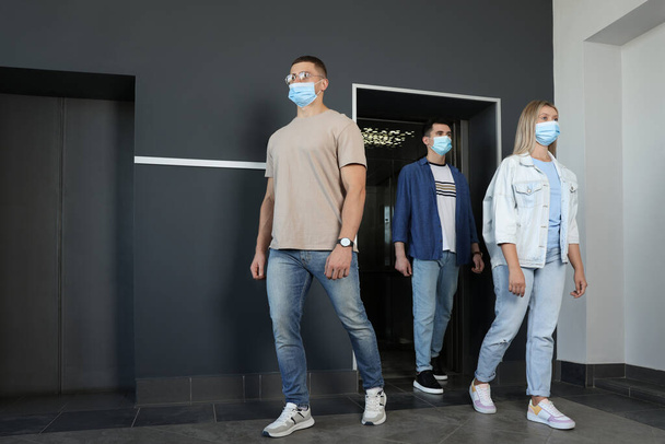 Group of people in face masks walking out from elevator. Protective measure - Foto, Bild