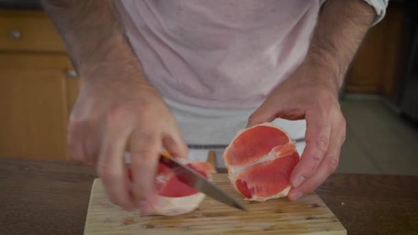 Разрезание красного грейпфрута и швыряние кусочков в миску с другими фруктами, готовыми к сжатию в медленной соковыжималке - Кадры, видео