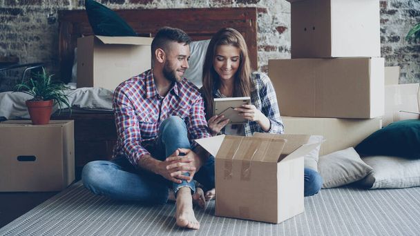 Happy couple is unpacking things after relocation opening carton box and looking at photos talking and laughing together. Moving to new house and relationship concept. - 写真・画像