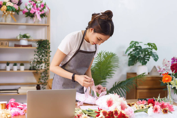 Flower shop concept, Female florist creating colorful flowers bouquet with paper and ribbon bow. - 写真・画像