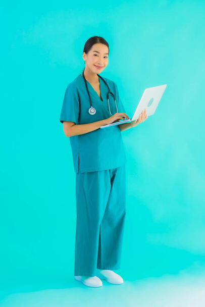 Retrato bonito jovem asiático médico mulher com laptop ou computador em azul isolado fundo
 - Foto, Imagem
