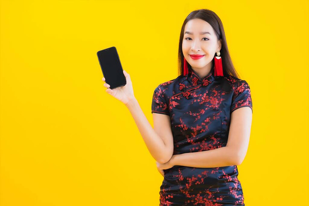 Porträt schöne junge asiatische Frau tragen chinesisches Kleid verwenden Smartphone für chinesische Neujahrskonzept auf gelbem Hintergrund isoliert - Foto, Bild