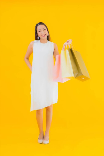 Portret mooie jonge aziatische vrouw met boodschappentas van retails warenhuis op geel geïsoleerde achtergrond - Foto, afbeelding