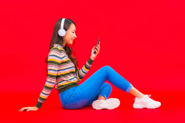 Retrato hermosa joven asiática mujer uso inteligente teléfono móvil con auriculares para escuchar música - Foto, Imagen