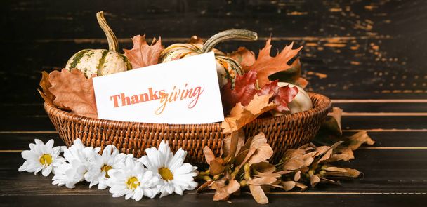 Cesta con calabazas, hojas de otoño y tarjeta sobre fondo de madera oscura. Celebración del Día de Acción de Gracias - Foto, imagen